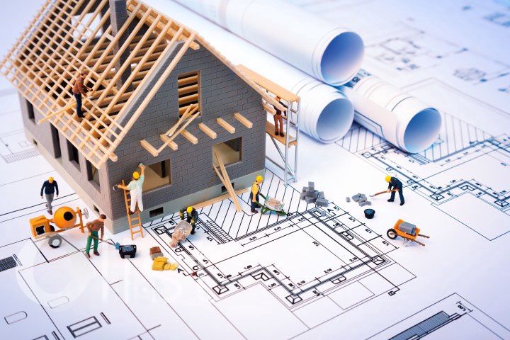 Miniature construction workers building a model house on top of architectural blueprints, representing services of construction companies in Nepal.
