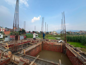 Foundation work in progress at an ST Builders construction site in Lalitpur with footing and column reinforcement.