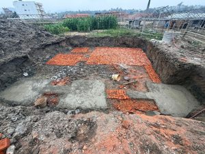 Foundation work at an ST Builders residential house construction site in Kathmandu, showing excavated pits with concrete footings and steel reinforcement.
