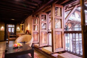 Traditional Nepali interior design featuring intricate wooden carved windows, a low wooden table with a fruit bowl, and warm lighting, showcasing a blend of cultural heritage and functional living space.